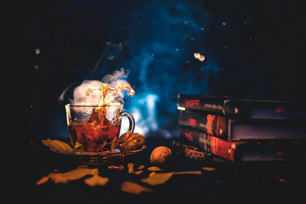 Stack of hardcover mystery novels beside a steaming cup of tea and reading glasses