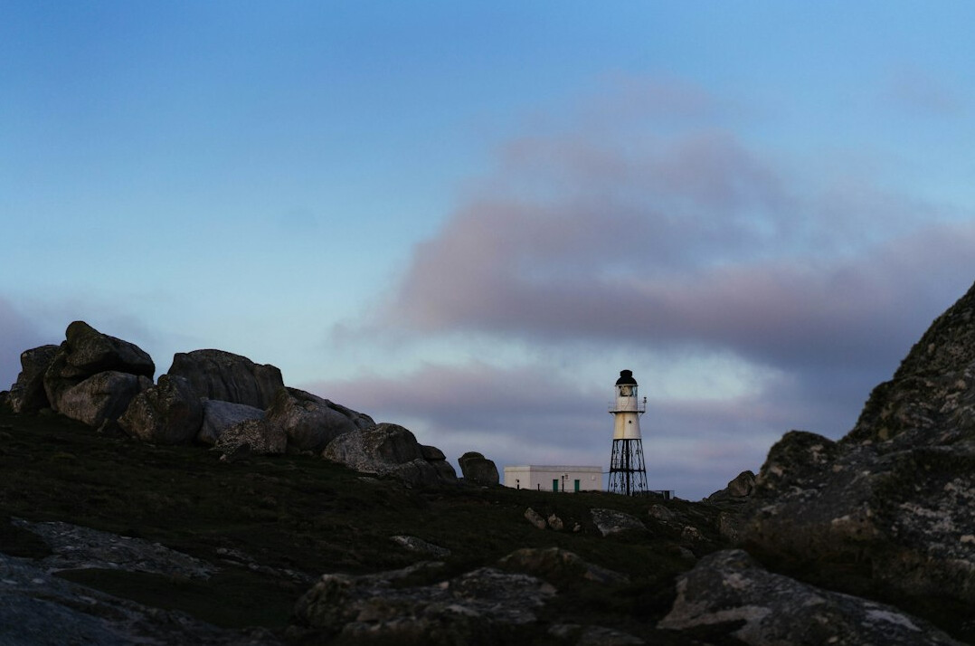 Lighthouse on a rocky coastline at dusk with a moody sky