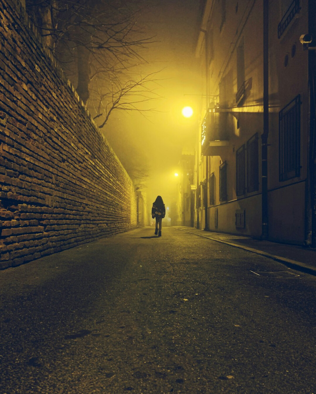 Silhouette of a person in a coat walking through a foggy street at night